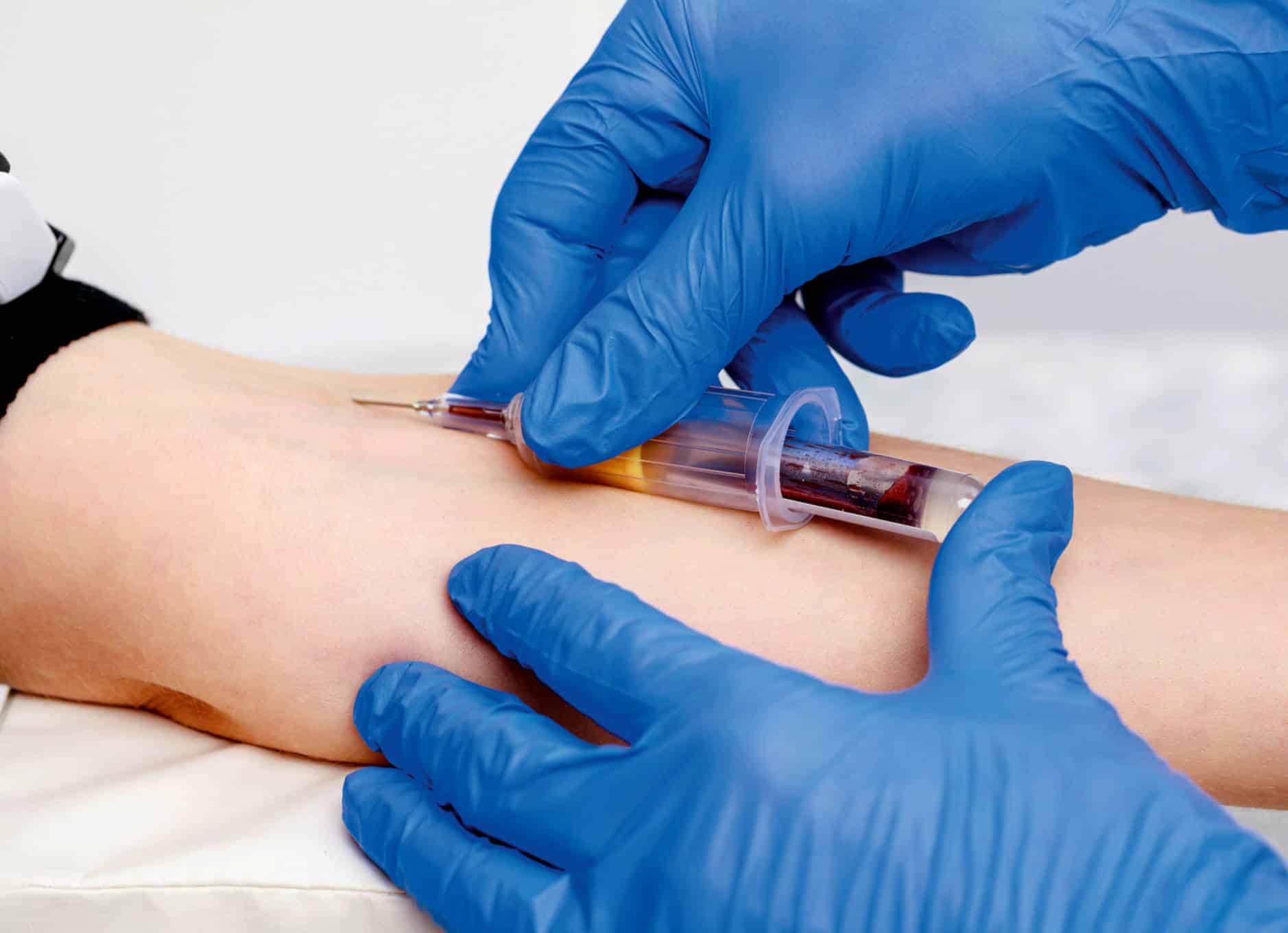 Henkilöön pistetään neula. Pistäjällä on käsissään suojakäsineet.