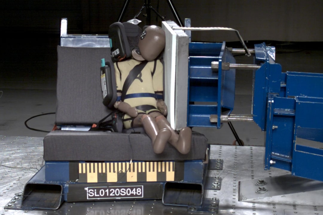 Testinukke turvaistuimessa sekä turvaistuimen testauslaitteistoa.