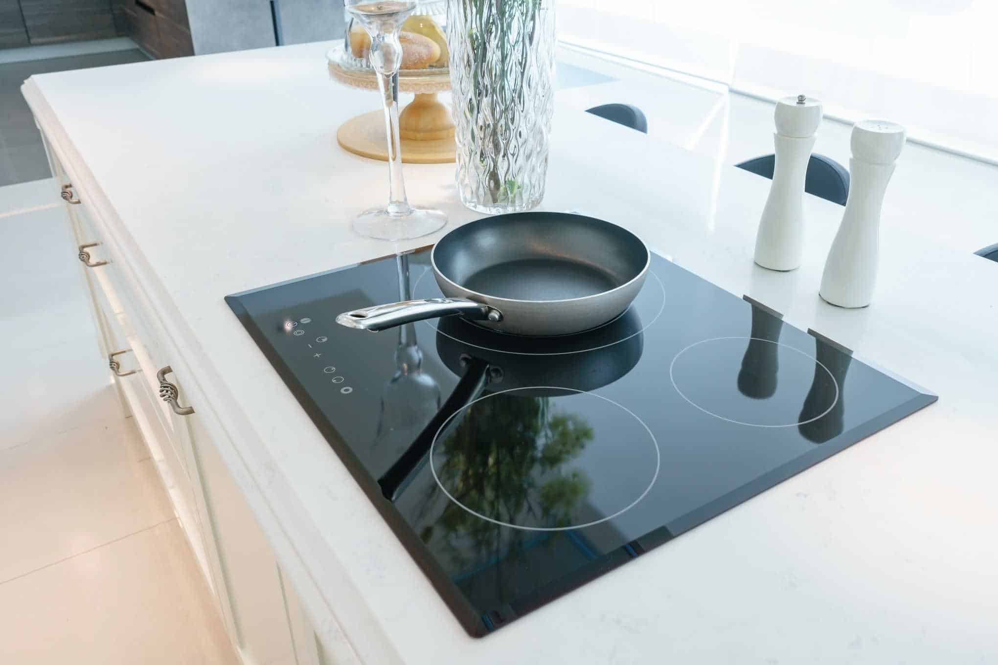 Keittiötaso, jolla on induktioliesi, paistinpannu, suolamylly, lasi ja maljakko.