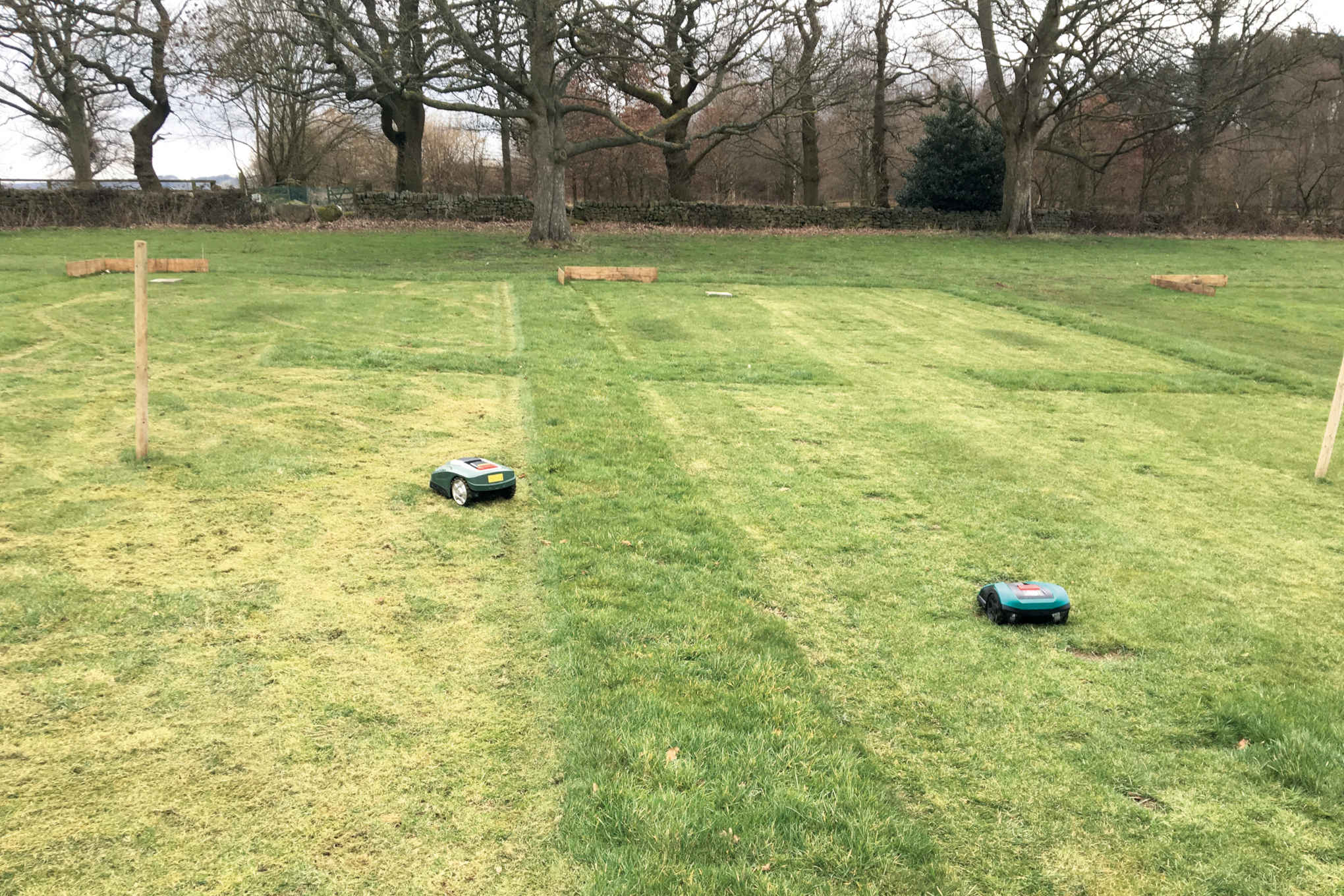 Kaksi robottiruohonleikkuria nurmikentällä.