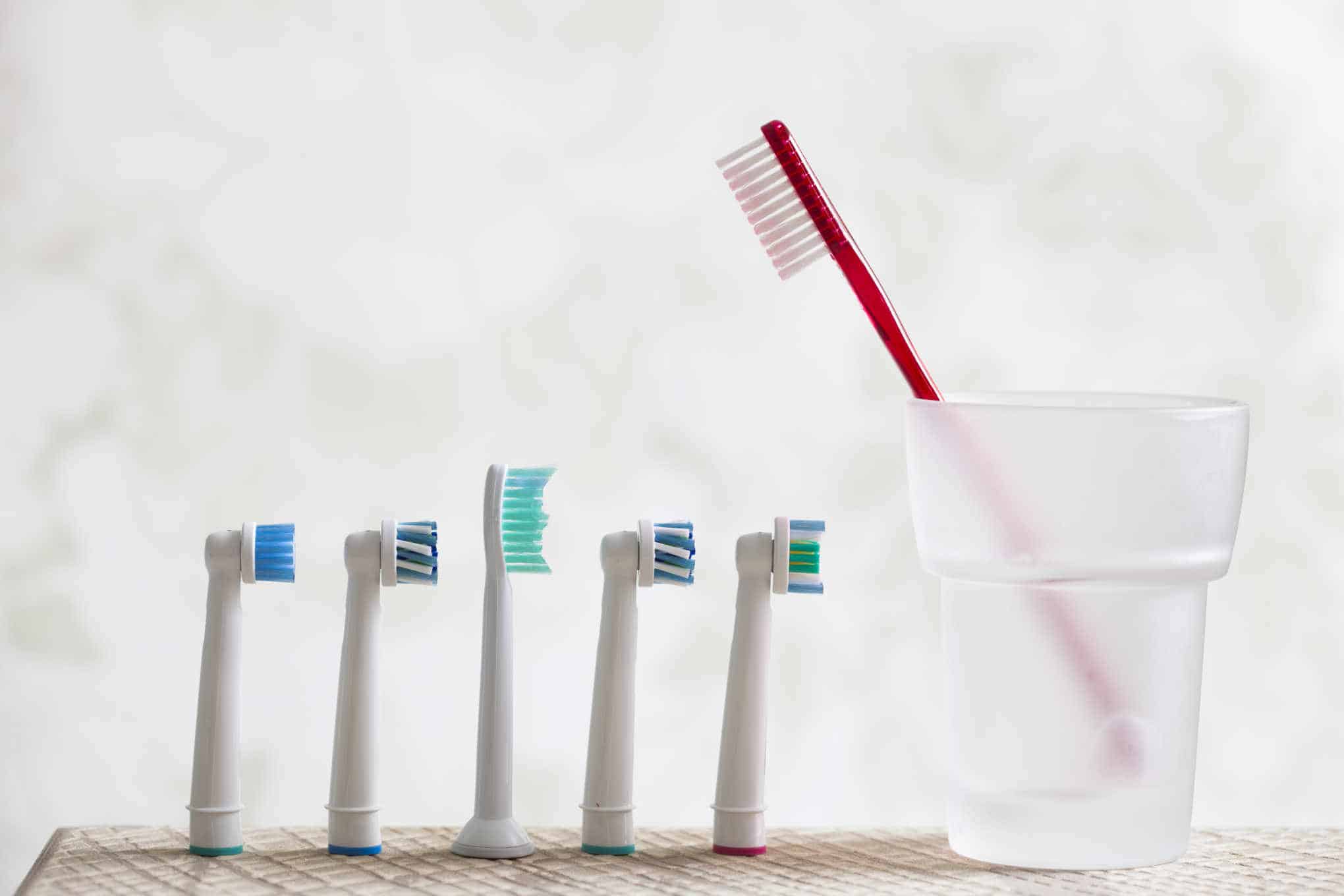 Käsikäyttöinen hammasharja muovimukissa ja useita sähköhammasharjan harjaspäitä.