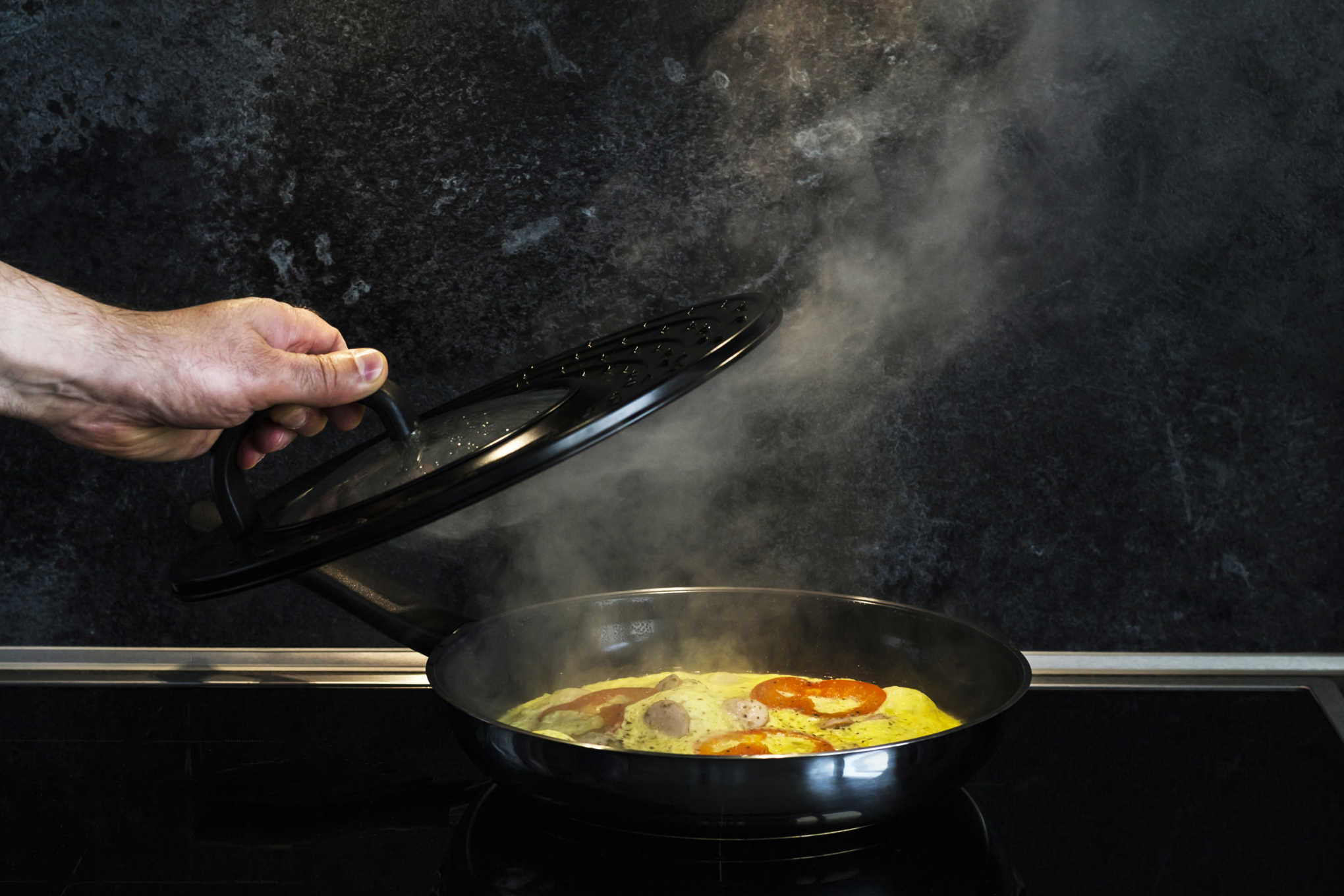 Paistinpannulla paistetaan ruokaa. Henkilö nostaa kannen paistinpannun päältä.