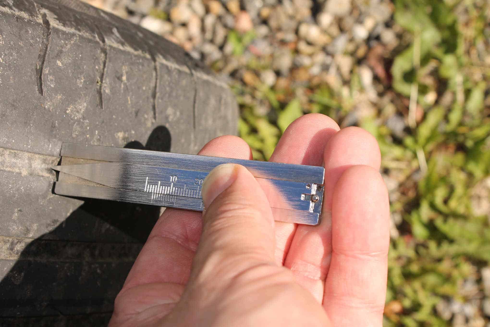 Henkilö mittaa mittarilla renkaan urasyvyyttä.