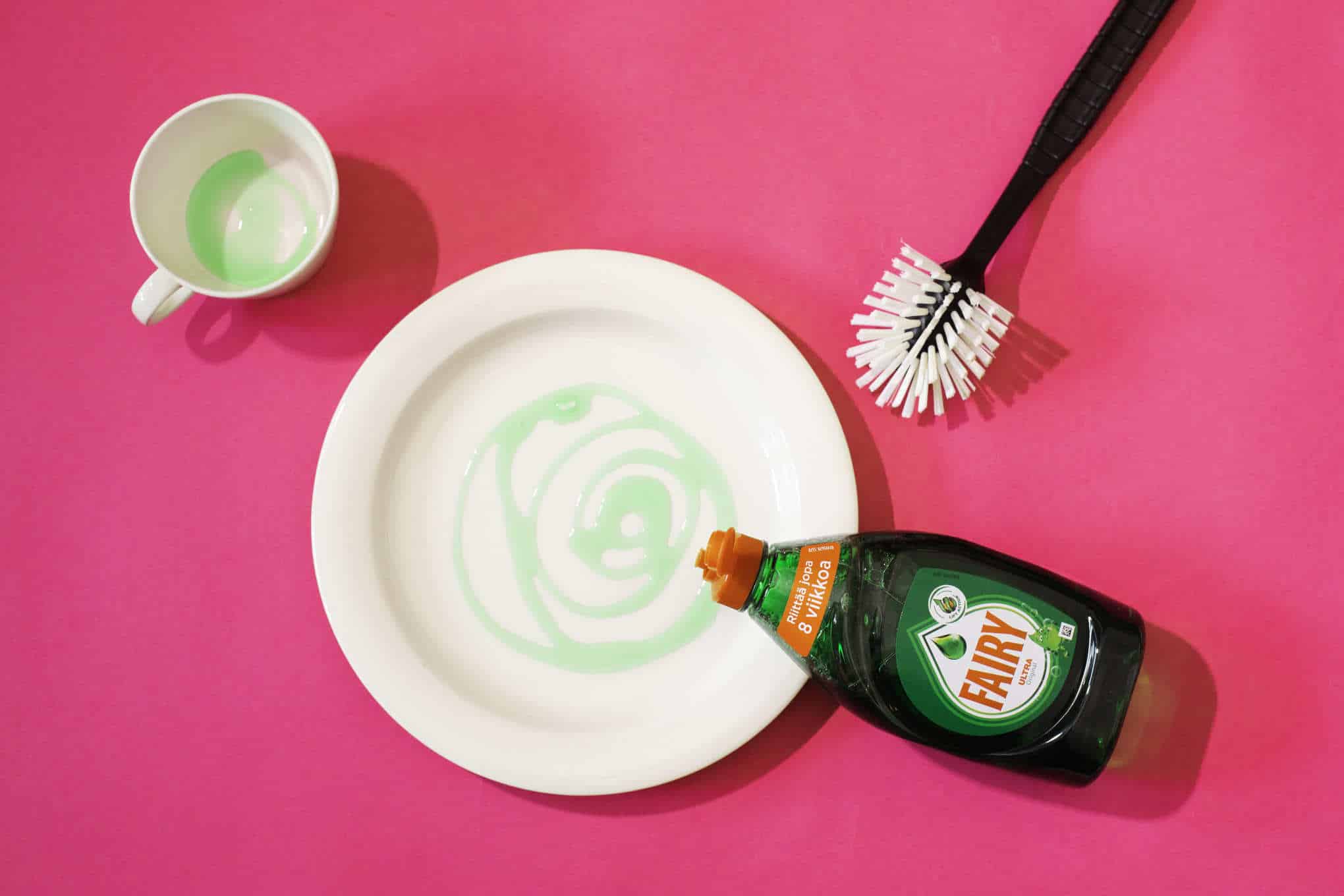 Kahvikuppi, lautanen, tiskiharja ja Fairy-merkkinen tiskiainepullo.