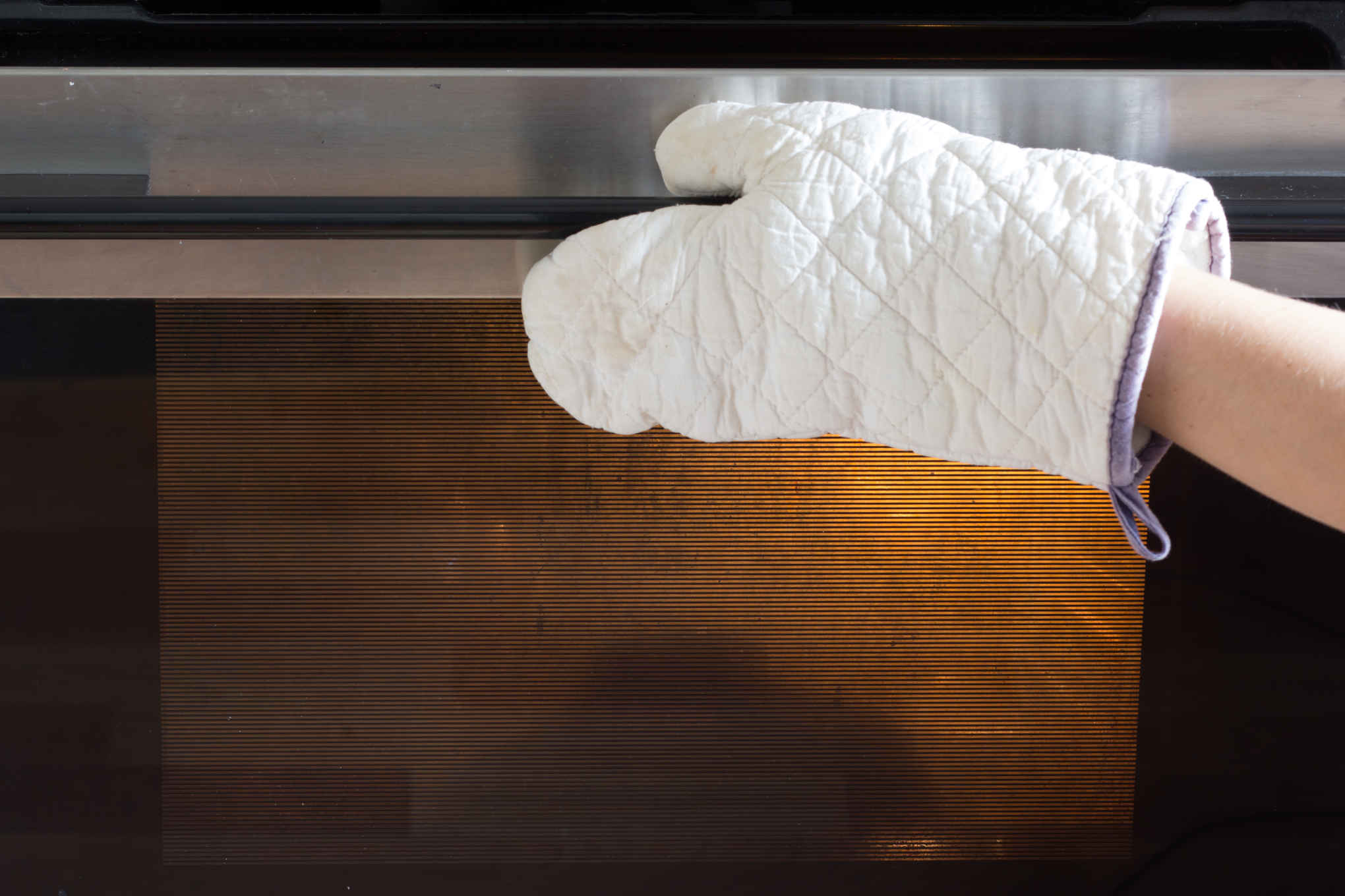 Henkilö avaa uunin luukkua patakintaalla.