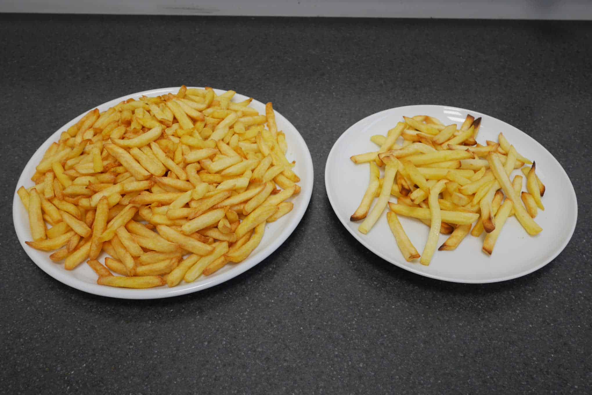 Kaksi lautasta, joista toisen päällä on paljon ja toisen päällä on vähän ranskalaisia perunoita.