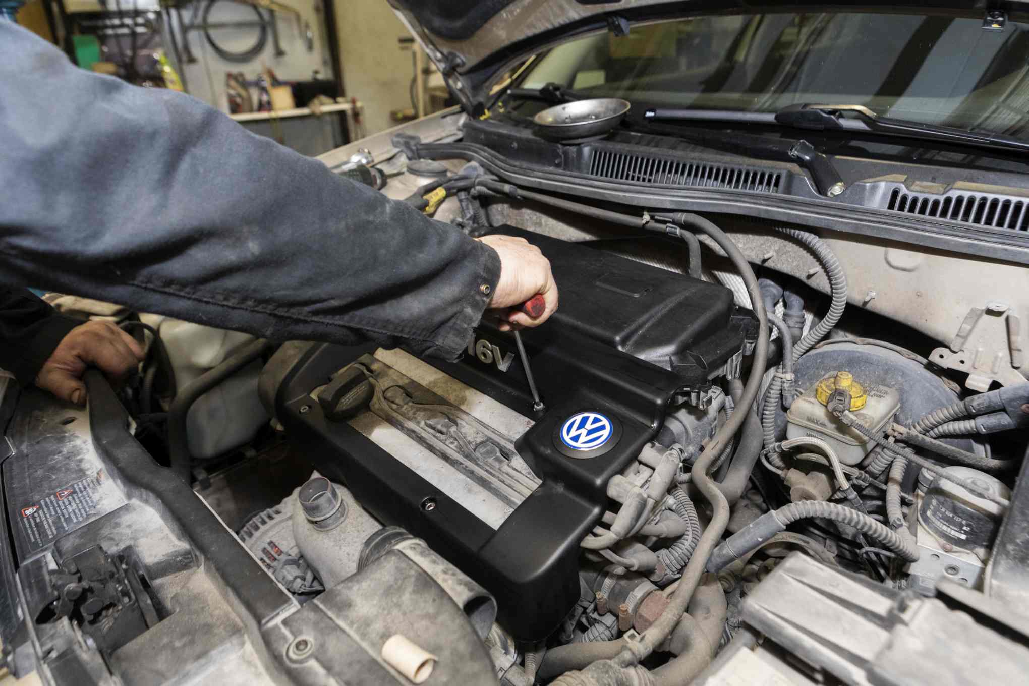 Henkilö korjaamassa Volkswagen-merkkisen auton moottoria.