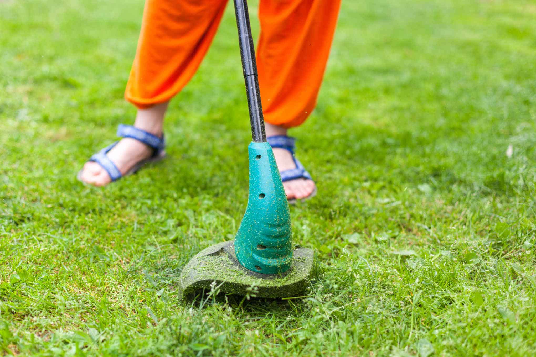 Henkilö leikkaamassa nurmikkoa ruohotrimmerillä.