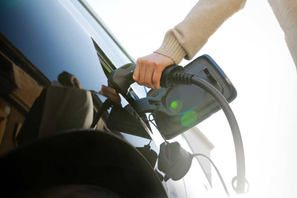 Henkilö laittamassa laturia sähköautoon.