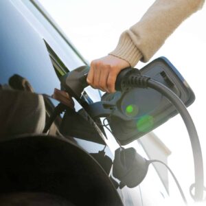 Henkilö laittamassa laturia sähköautoon.