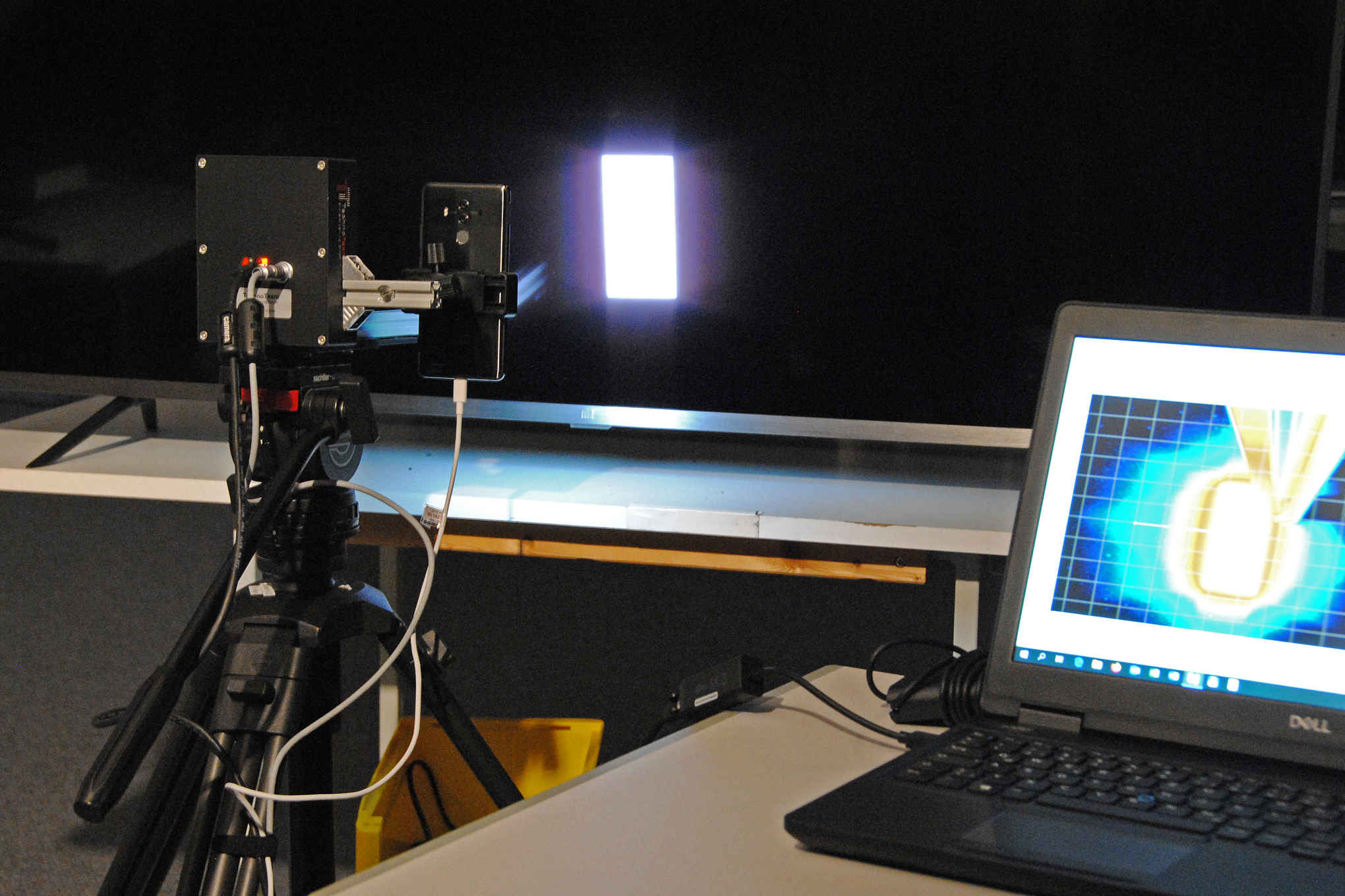 Televisio, tietokone ja puhelin, jonka näytöltä heijastetaan valoa televisioon.