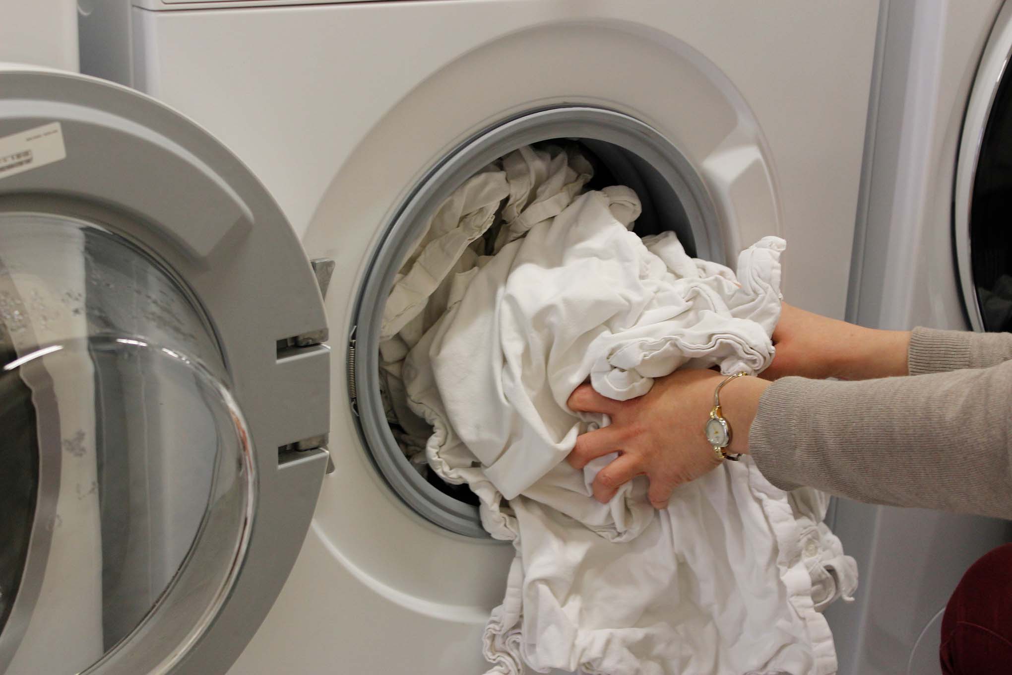 Henkilö laittamassa pyykkejä kuivausrumpuun