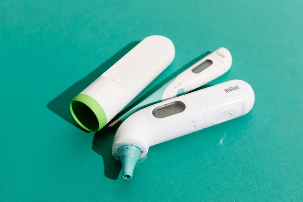 Perinteinen digitaalinen kuumemittari sekä korvaan asetettava kuumemittari.