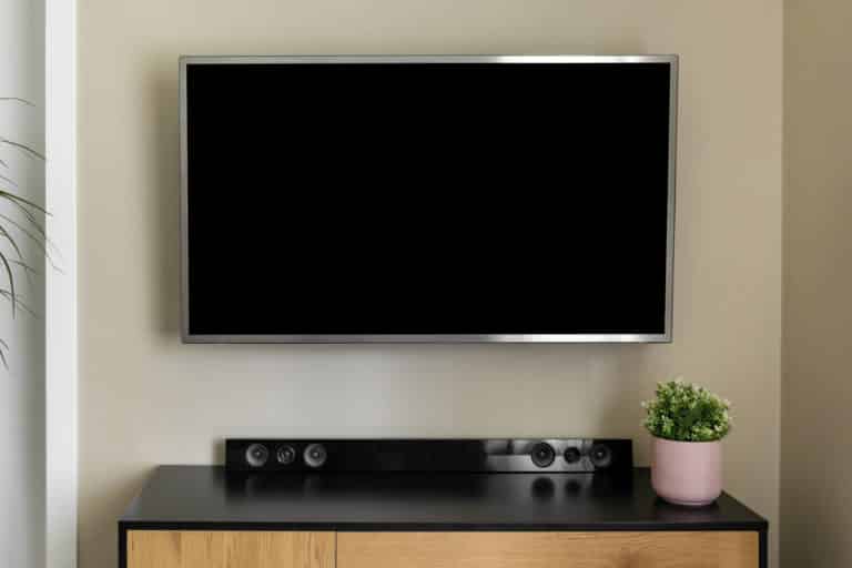 Seinään kiinnitetty televisio ja televisiotaso, jonka päällä on soundbar-kaiutin.