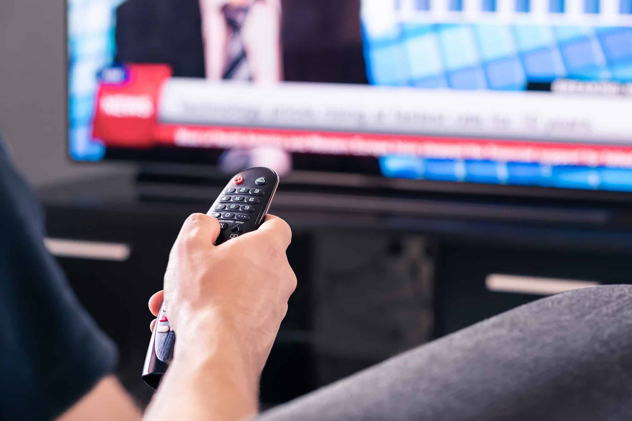 Henkilö, jolla on kädessään kaukosäädin katsoo televisiota.