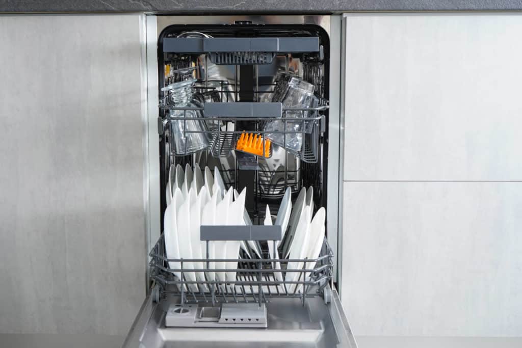 Auki oleva kapea astianpesukone, jonka sisällä on puhtaita astioita.
