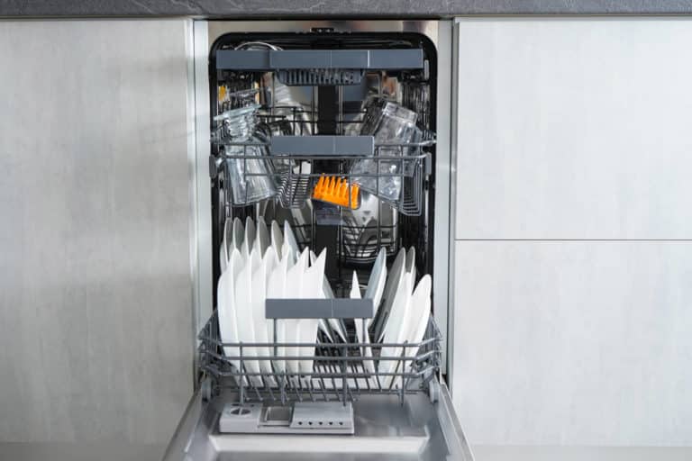 Auki oleva kapea astianpesukone, jonka sisällä on puhtaita astioita.