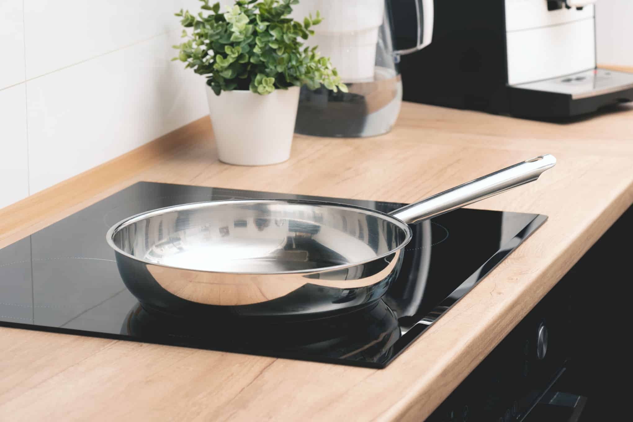 Induktiotaso, jonka päällä on paistinpannu, ja jonka vieressä on huonekasvi.