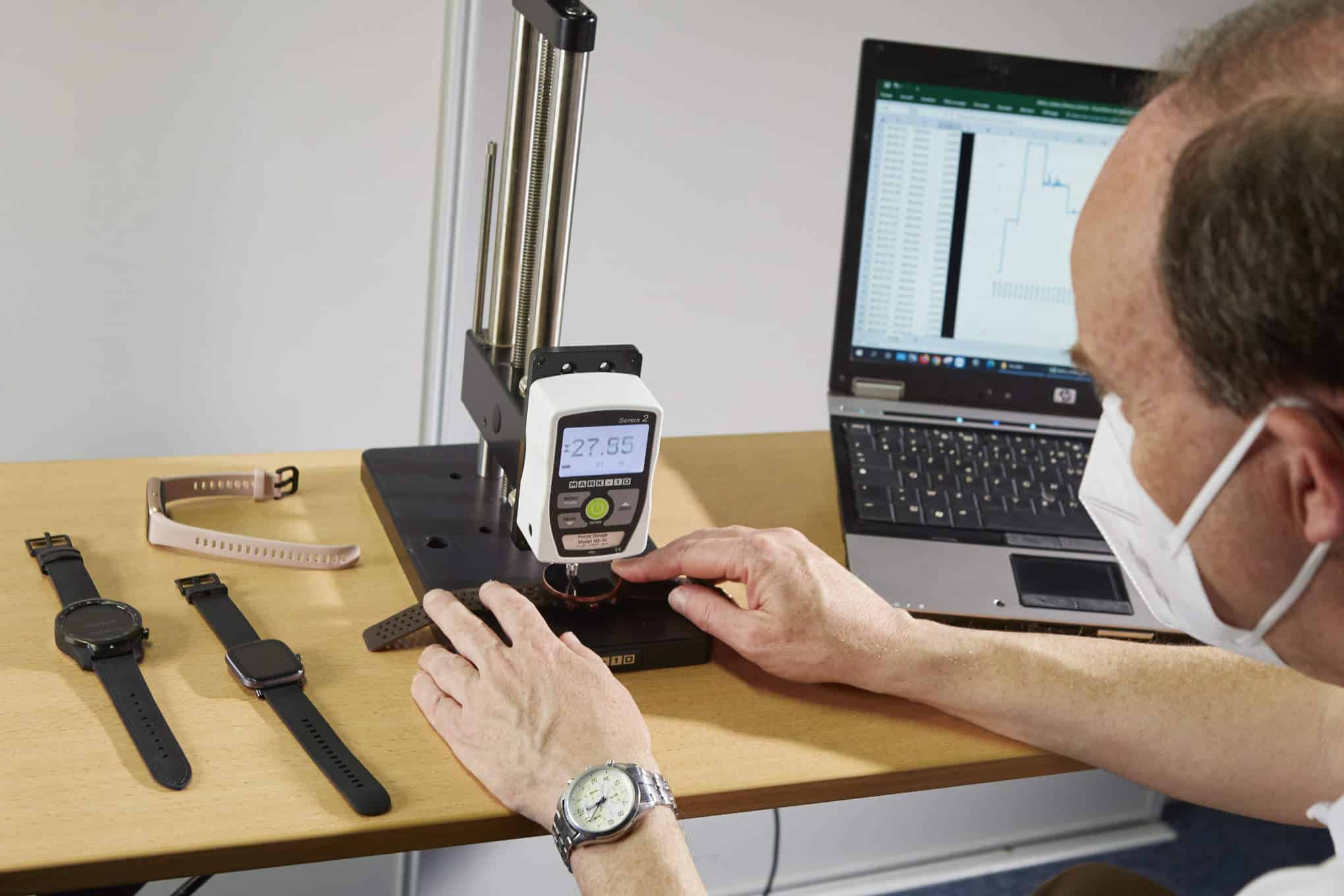 Henkilö testaamassa aktiivisuusrannekkeiden naarmuuntumisherkkyyttä testauslaitteella.