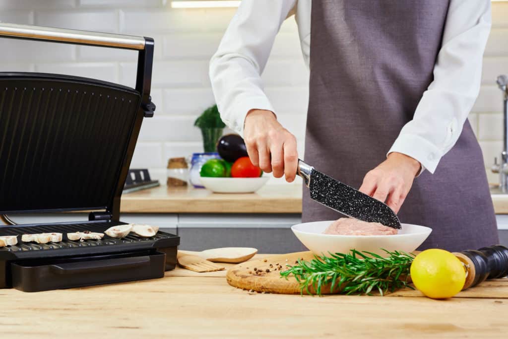 Pöytägrilli, jonka vieressä on henkilö laittamassa ruokaa.