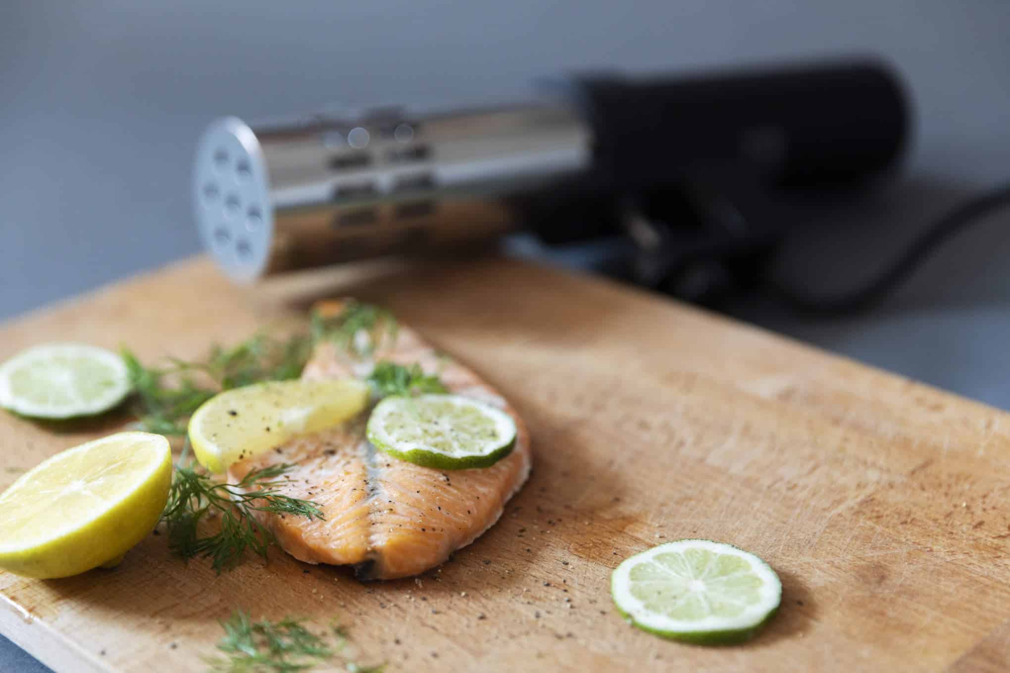 Leikkuulauta, jonka päällä on sous vide -sirkulaattori, lohimedaljonki, tilliä ja sitruunaviipaleita