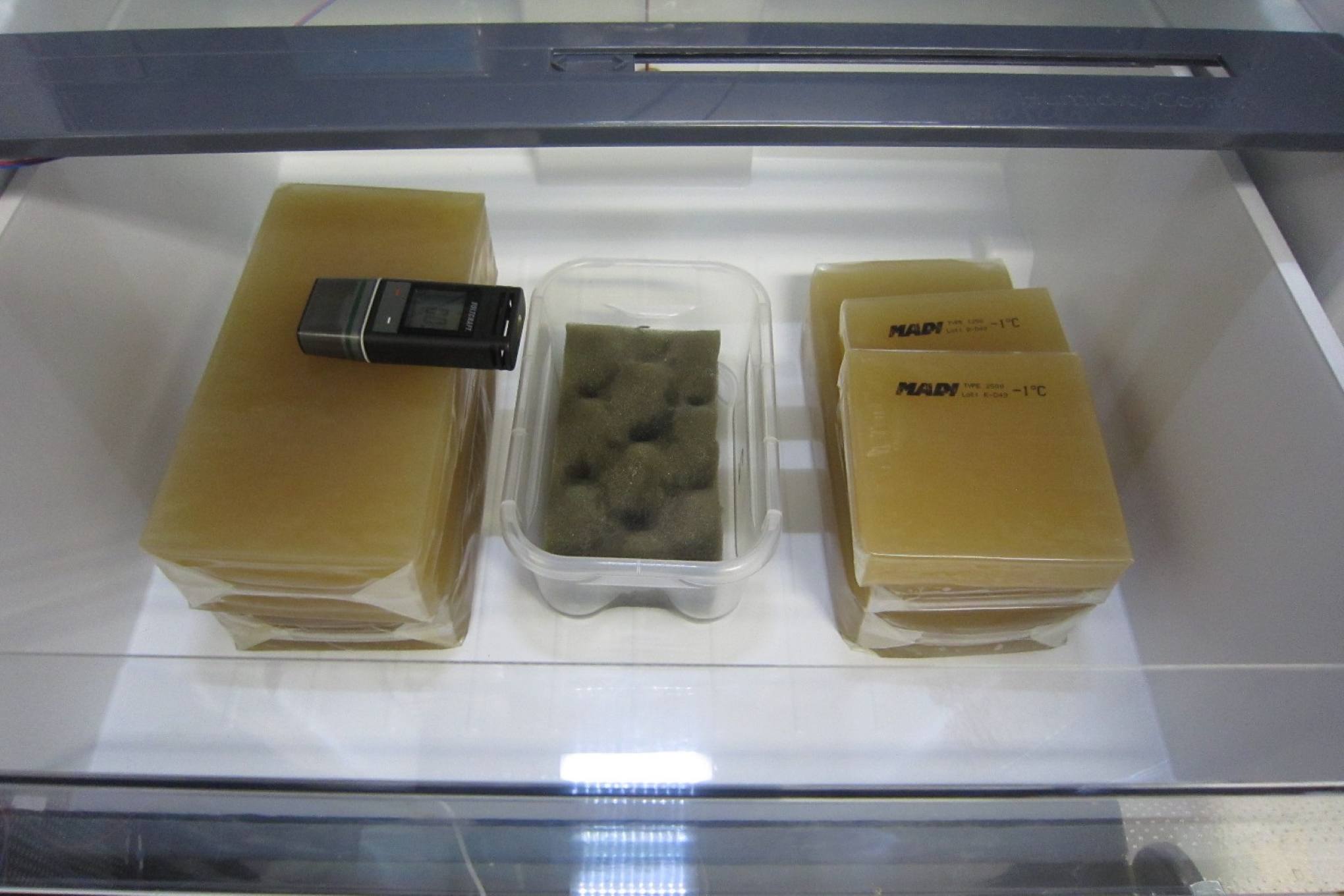 Jääkaapin vihanneslaatikko, jossa on elintarvikkeita simuloivia pakkauksia ja testauslaitteistoa.