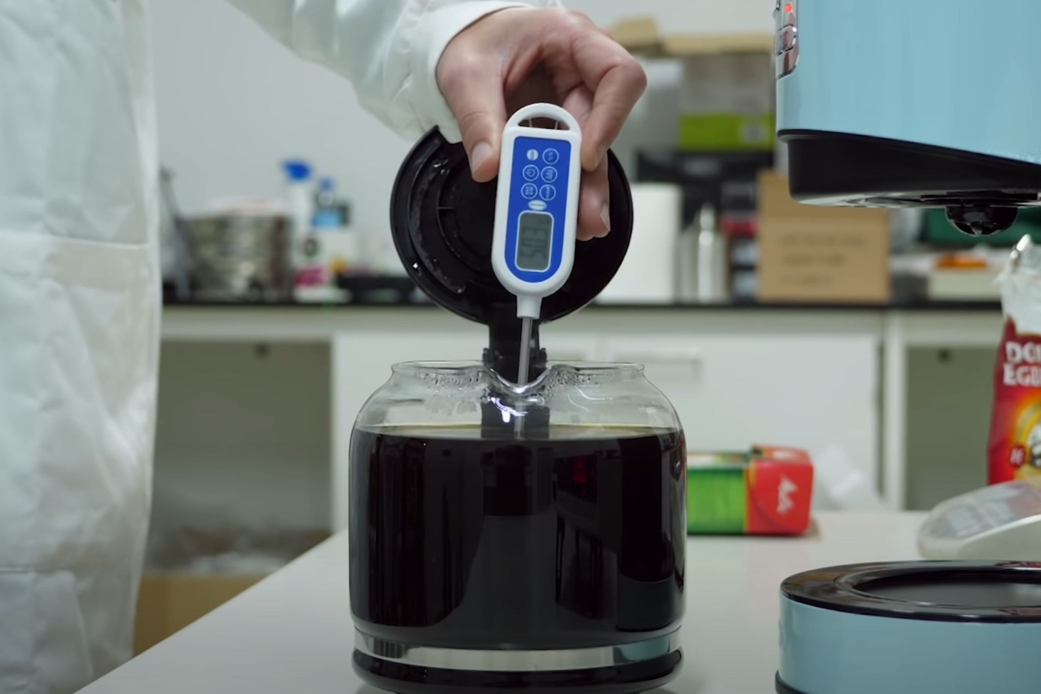 Henkilö mittaamassa kahvipannussa olevan kahvin lämpötilaa lämpömittarilla.