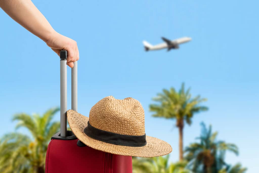 Matkalaukkua pitelevä henkilö katsoo taivalla lentävää lentokonetta.