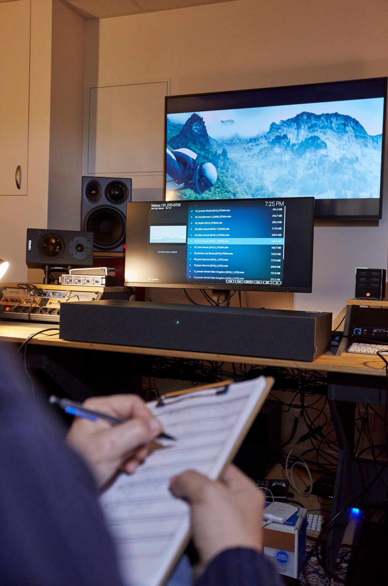 Henkilö istuu huoneessa, jossa on kaiuttimia ja elektroniikkaa.