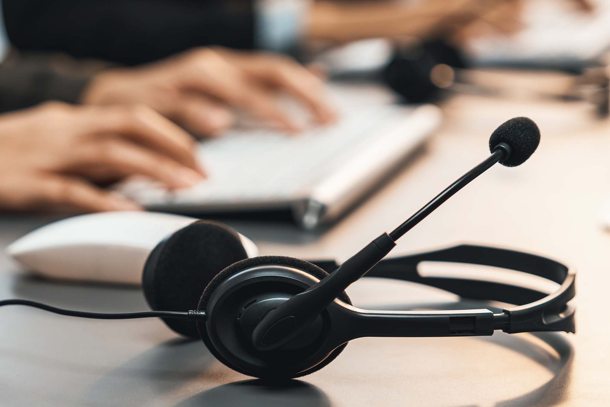 Henkilö käyttämässä tietokonetta, tietokoneen hiiri ja kuulokkeet, joissa on mikrofoni.