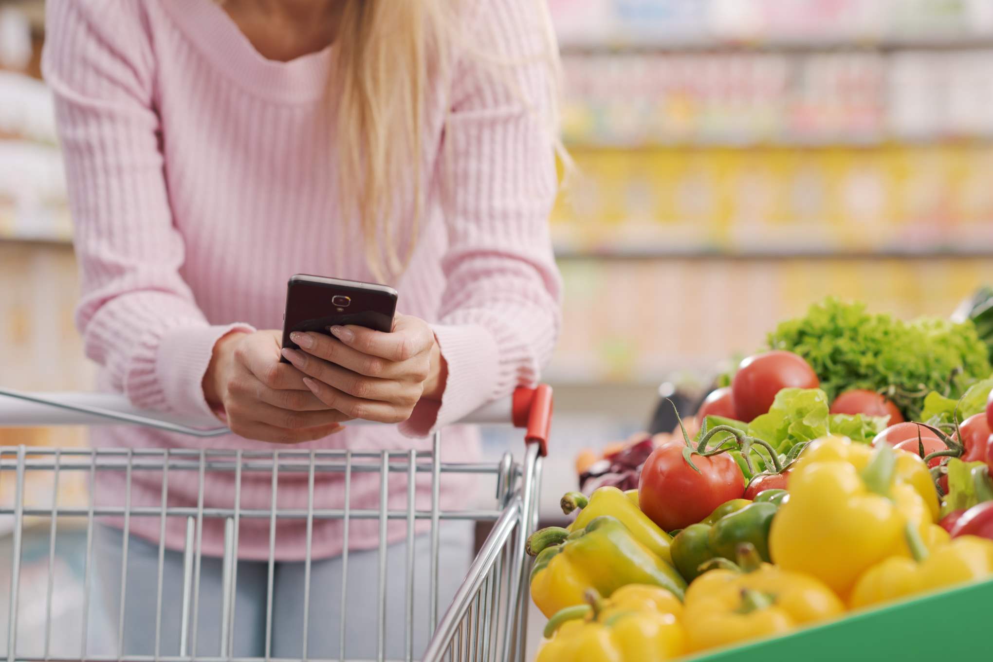 Henkilö käyttää puhelinta ruokakaupassa.