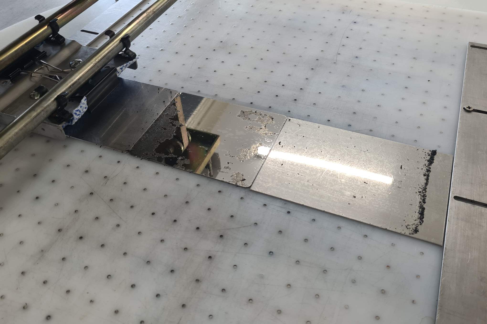 Metallisia testikappaleita kiinnitettynä pöytään ja testauslaitteistoa.