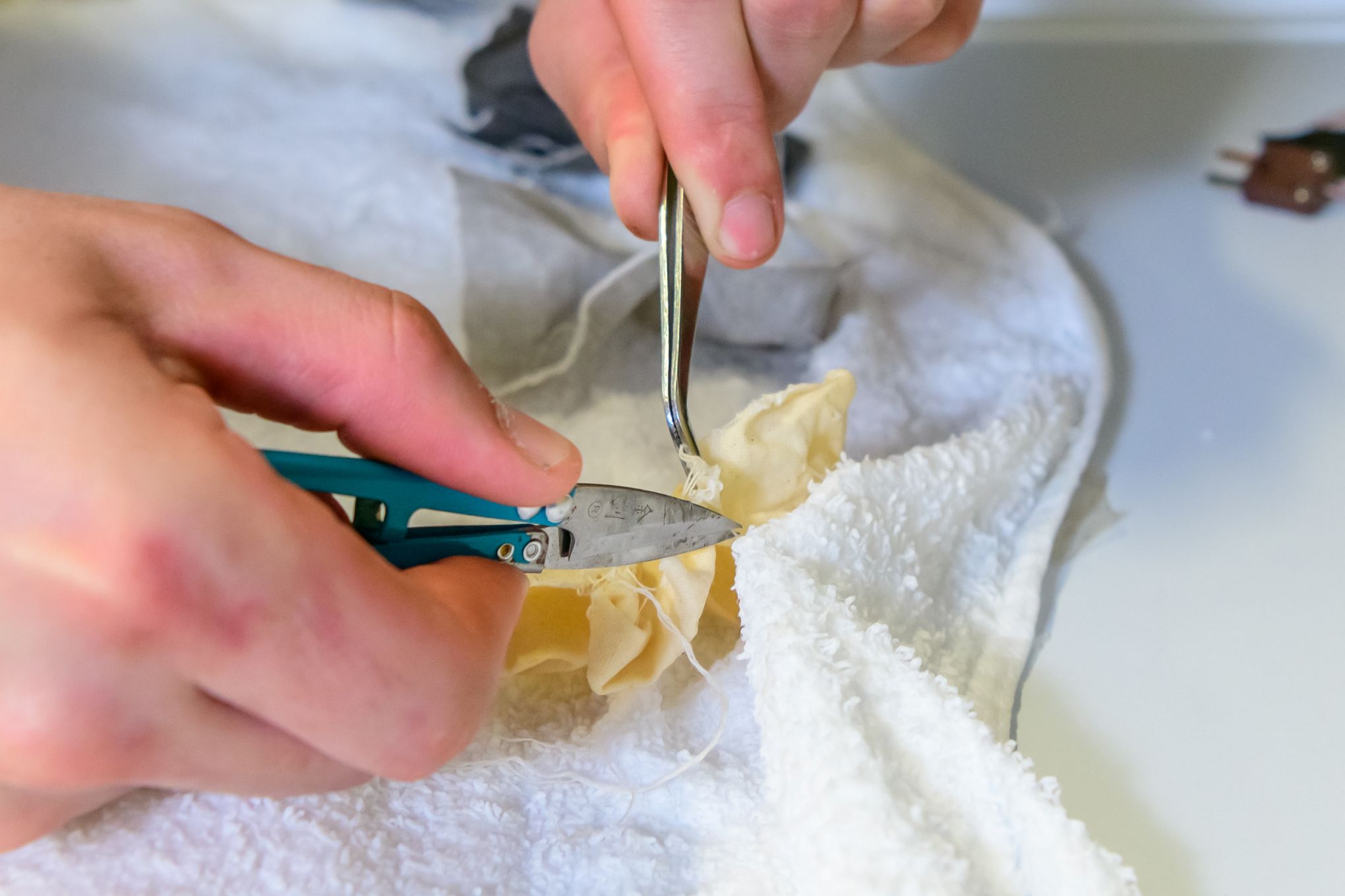 Henkilöllä on kädessään työkaluja ja kangasta.