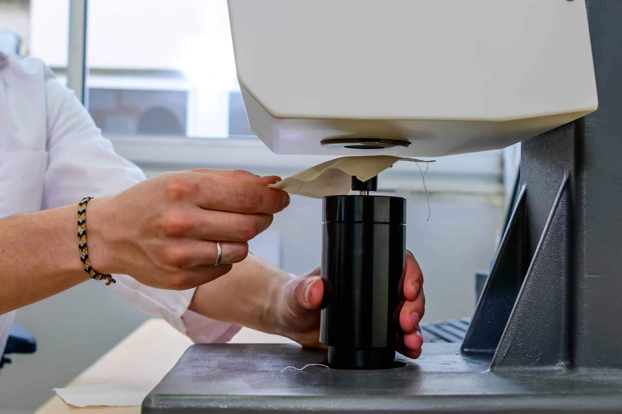 Testauslaitteistoa ja henkilö, jolla on kädessään tekstiilikappale.