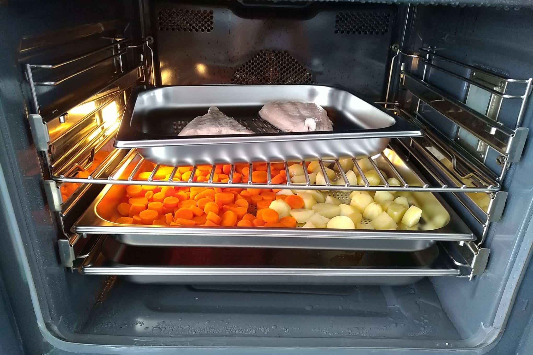 Auki oleva uuni, jonka sisällä on lohifileitä, perunoita ja porkkanoita.