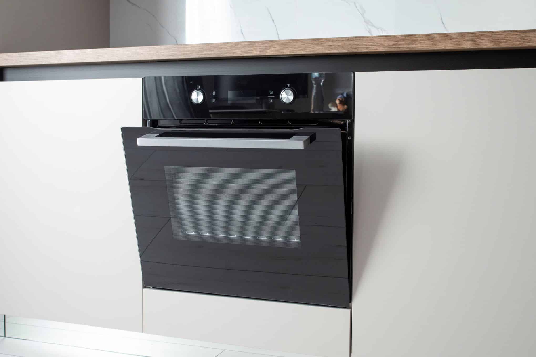 Kalusteisiin asennettu uuni, jonka luukku on raollaan.