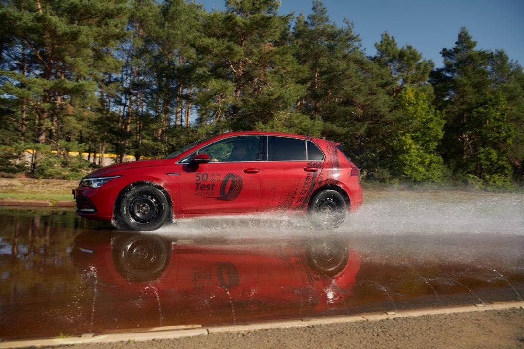 Punainen Volkswagen-merkkinen henkilöauto, jolla ajetaan märällä ajoradalla.