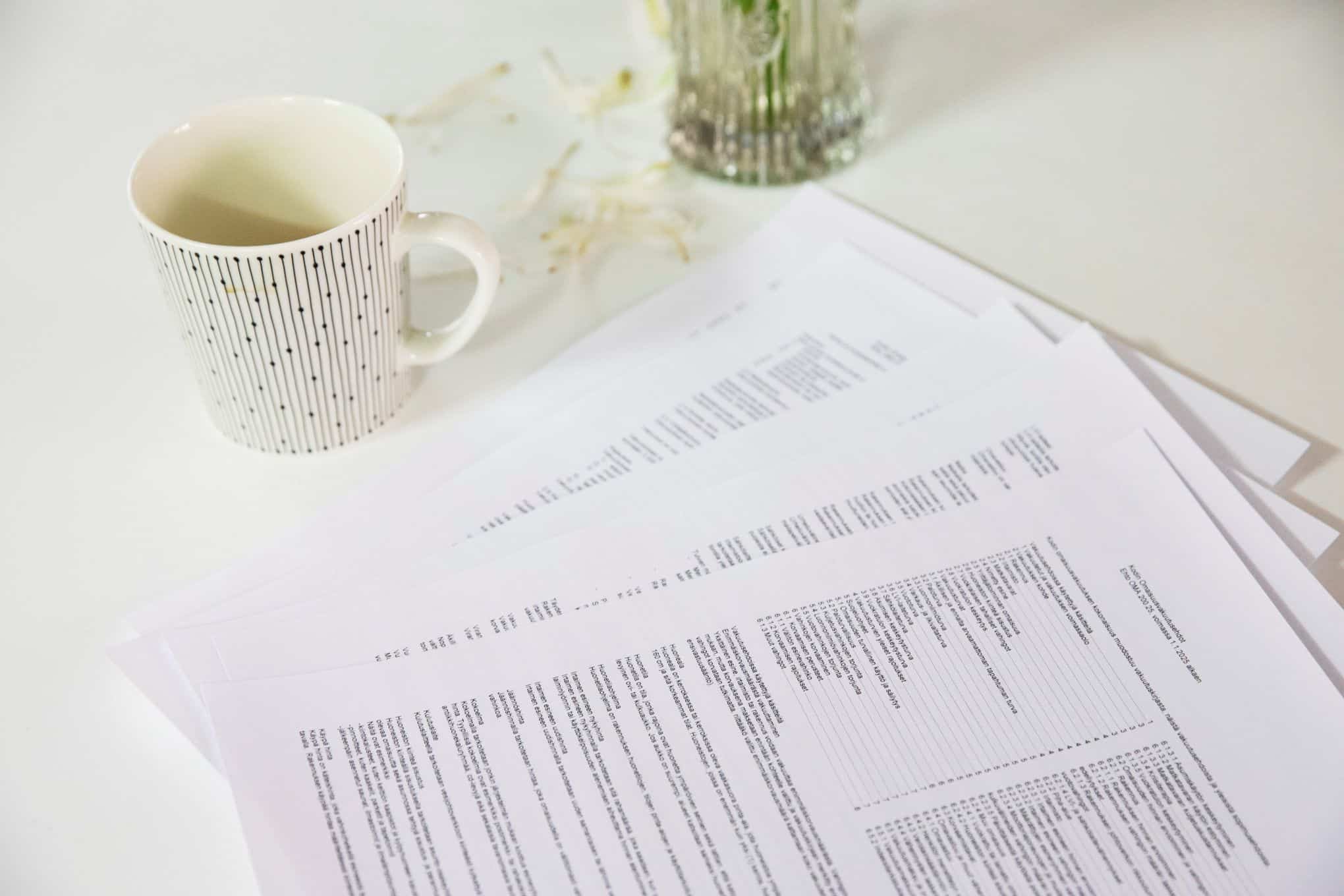 Pöydällä on vakuutusasiakirjoja ja kahvikuppi.