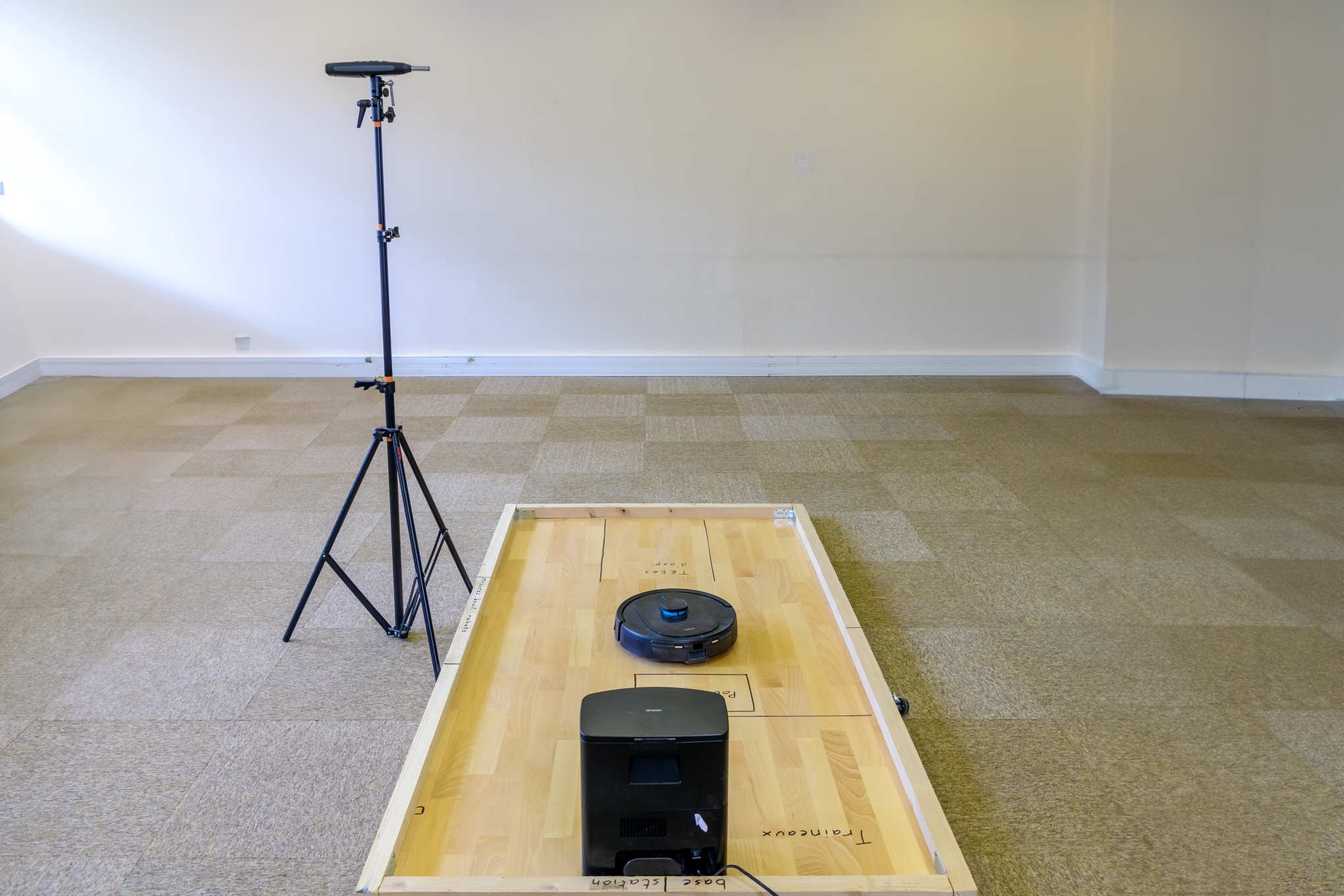 Lattialla on puualusta, robotti-imuri, tyhjennysasema ja desibelimittari.