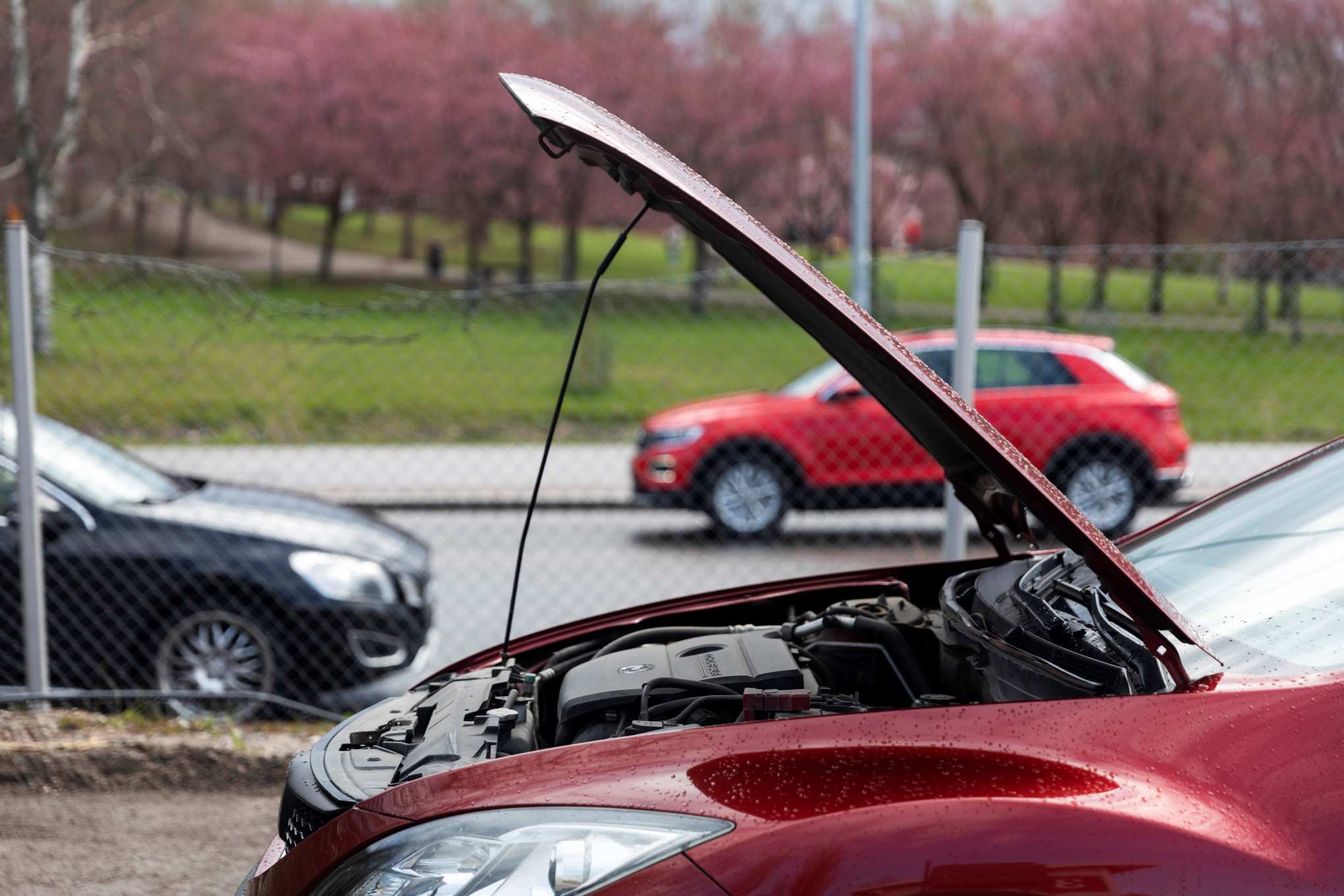 Punainen auto, jonka konepelti on auki. Taka-alalla on kaksi muuta autoa.