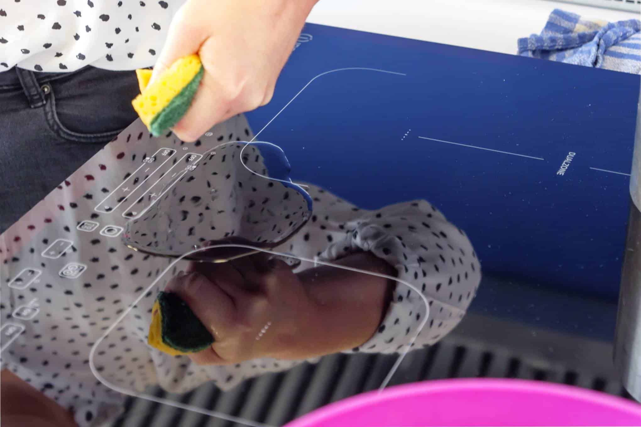 Induktiotaso, jonka päällä on vettä ja henkilö, ja henkilö, jolla on kädessään pesusieni.