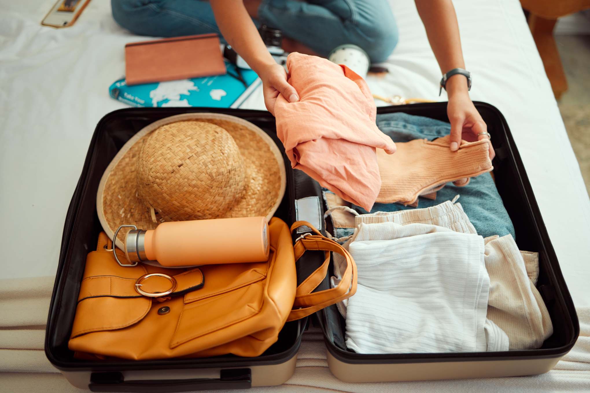 Matkalaukku, jossa on vaatteita, reppu, hattu ja juomapullo.