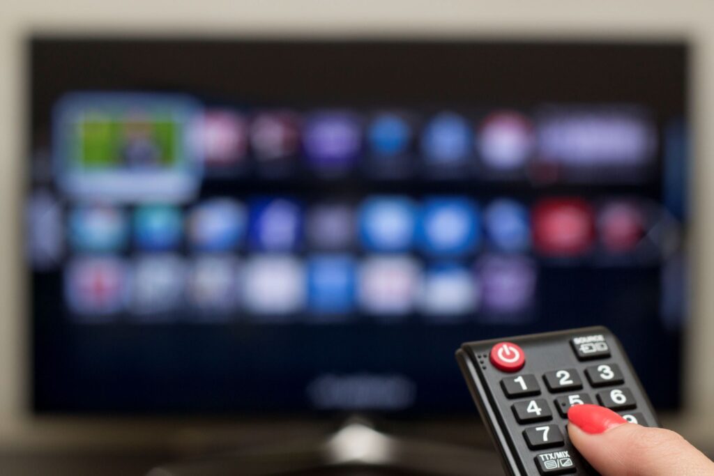 Henkilö osoittaa kaukosäätimellä televisiota.