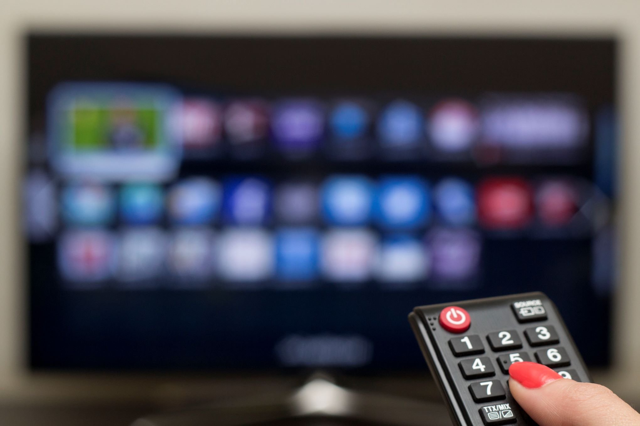 Henkilö osoittaa kaukosäätimellä televisiota.