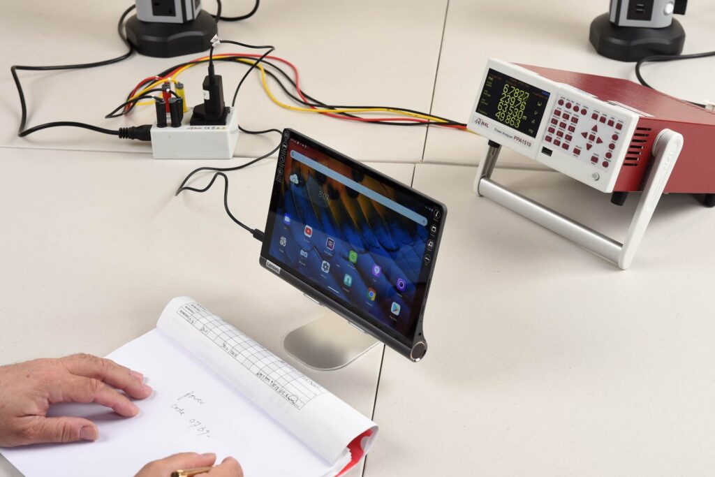 Tabletti, testauslaitteistoa ja henkilö, joka kirjoittaa muistiinpanoja vihkoon.