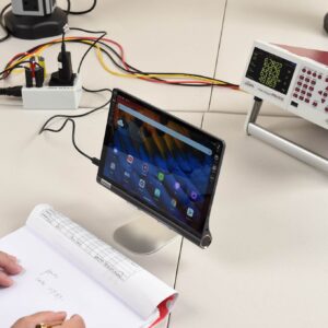 Tabletti, testauslaitteistoa ja henkilö, joka kirjoittaa muistiinpanoja vihkoon.