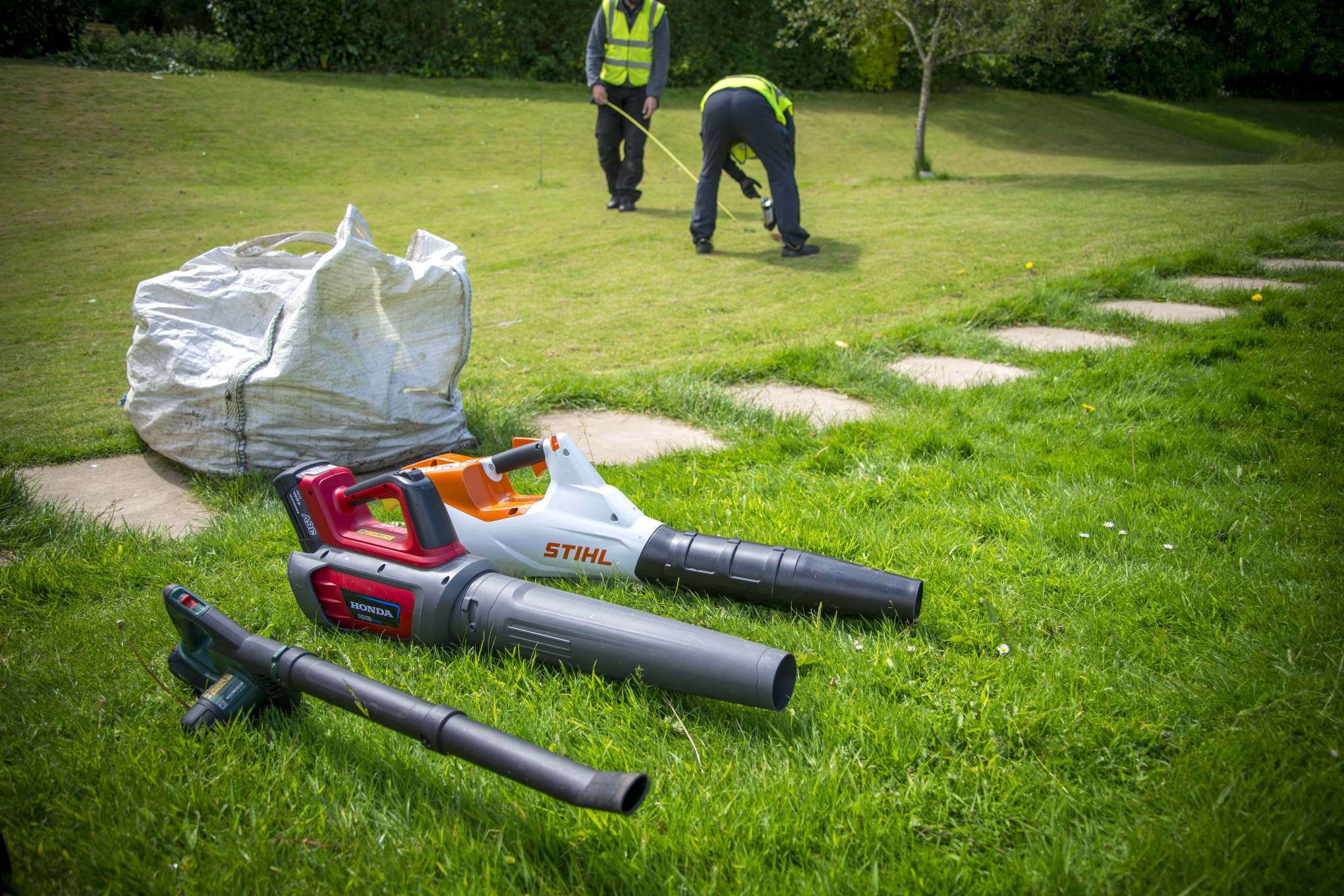 Kolme lehtipuhallinta nurmikolla.