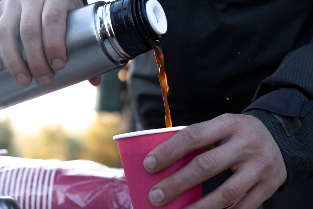 Henkilö kaataa kahvia termospullosta pahvimukiin.