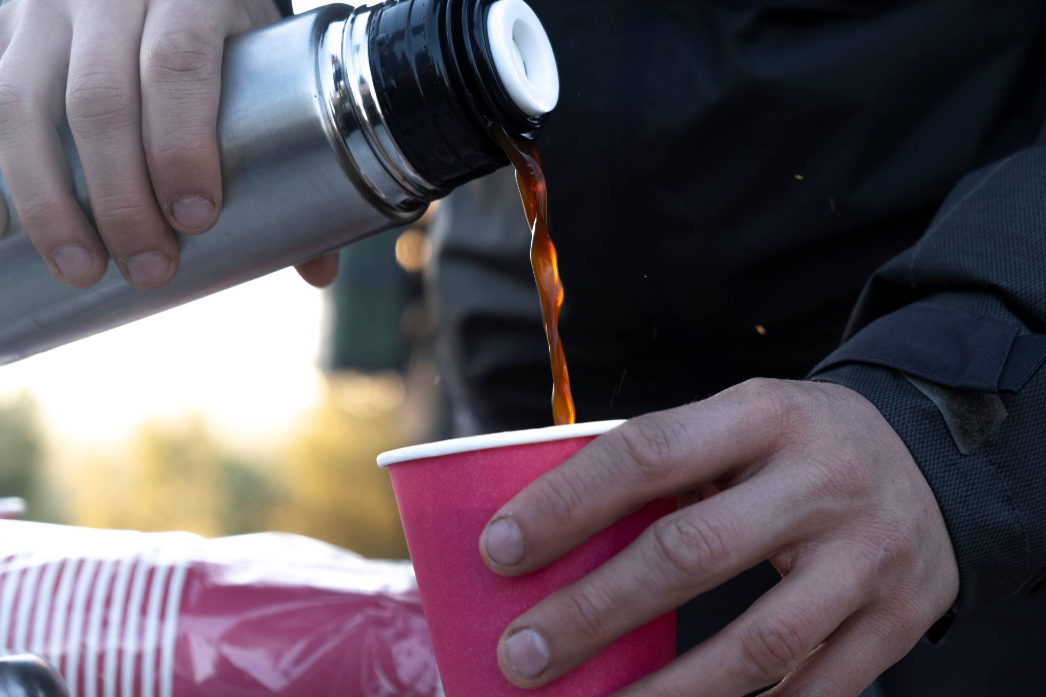 Henkilö kaataa kahvia termospullosta pahvimukiin.