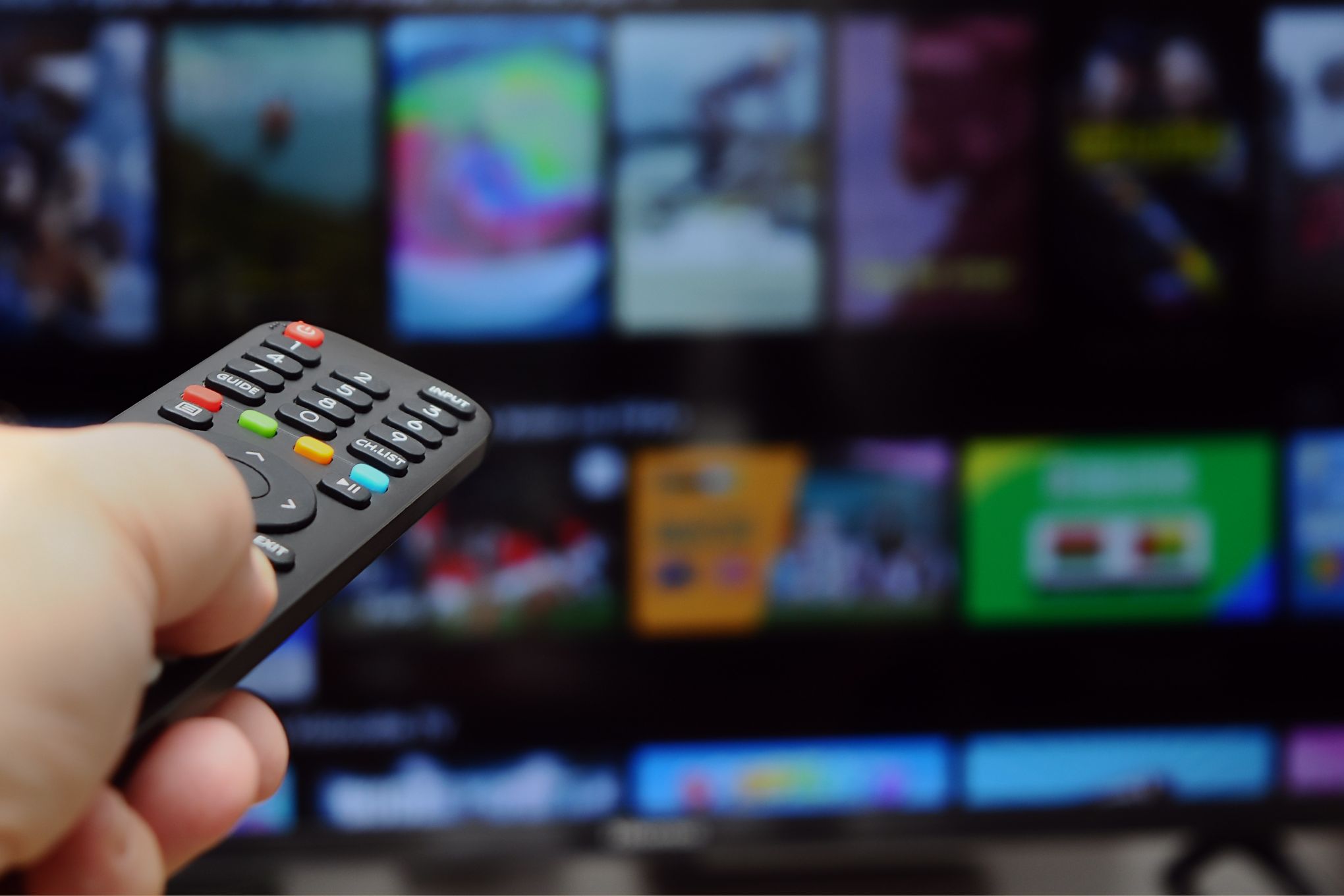 Henkilö osoittaa kaukosäätimellä televisiota.